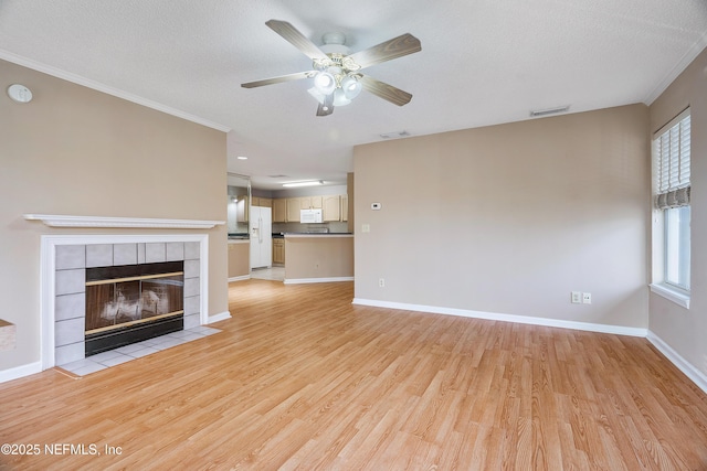 unfurnished living room featuring a tiled fireplace, crown molding, a textured ceiling, and light hardwood / wood-style flooring