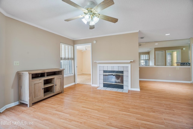 unfurnished living room with a tiled fireplace, ceiling fan, light hardwood / wood-style floors, crown molding, and a textured ceiling