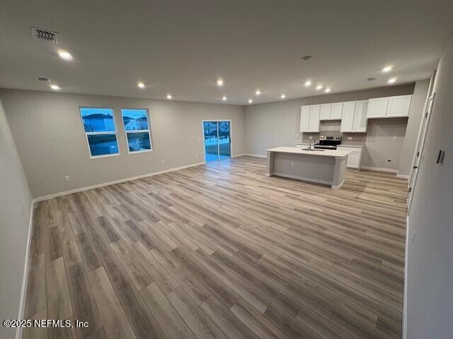 kitchen featuring sink, white cabinetry, electric range, a kitchen island with sink, and light hardwood / wood-style floors