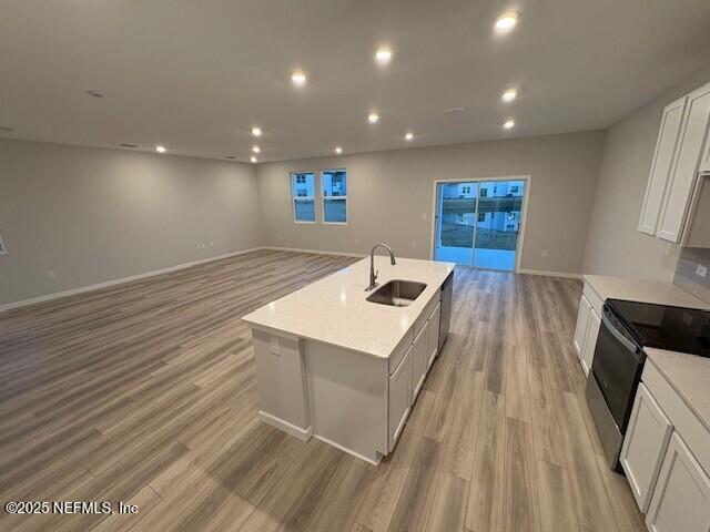 kitchen featuring range with electric stovetop, an island with sink, sink, white cabinets, and light hardwood / wood-style floors