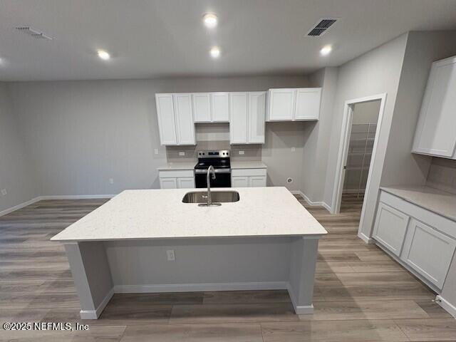 kitchen with white cabinetry, sink, stainless steel electric range, and a center island with sink