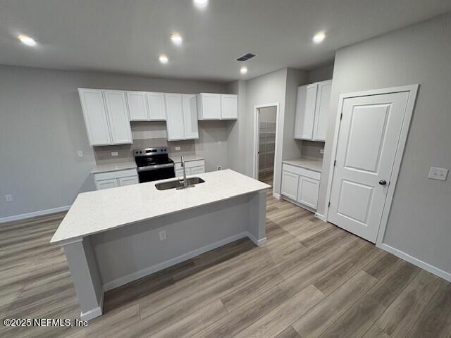 kitchen featuring stainless steel electric range oven, sink, white cabinets, a center island with sink, and light wood-type flooring