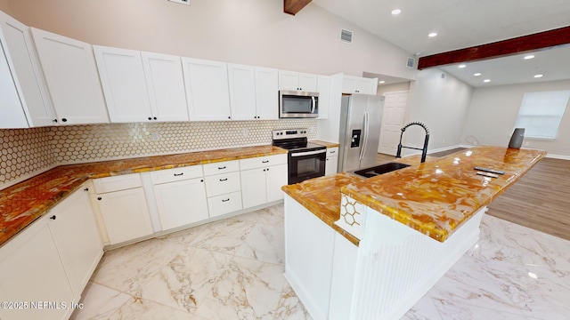 kitchen featuring appliances with stainless steel finishes, white cabinetry, vaulted ceiling with beams, a center island, and tasteful backsplash