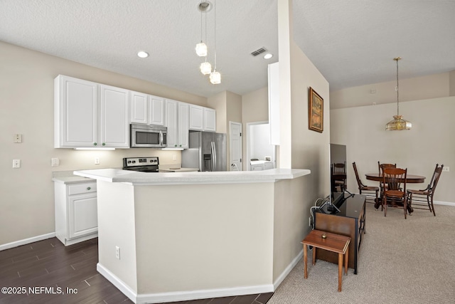 kitchen with white cabinetry, appliances with stainless steel finishes, kitchen peninsula, and pendant lighting