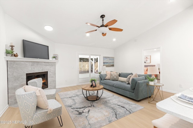 living room with vaulted ceiling, a premium fireplace, ceiling fan, and light wood-type flooring