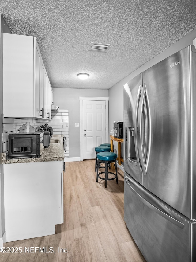 kitchen with stainless steel fridge, dark stone countertops, tasteful backsplash, white cabinets, and light wood-type flooring