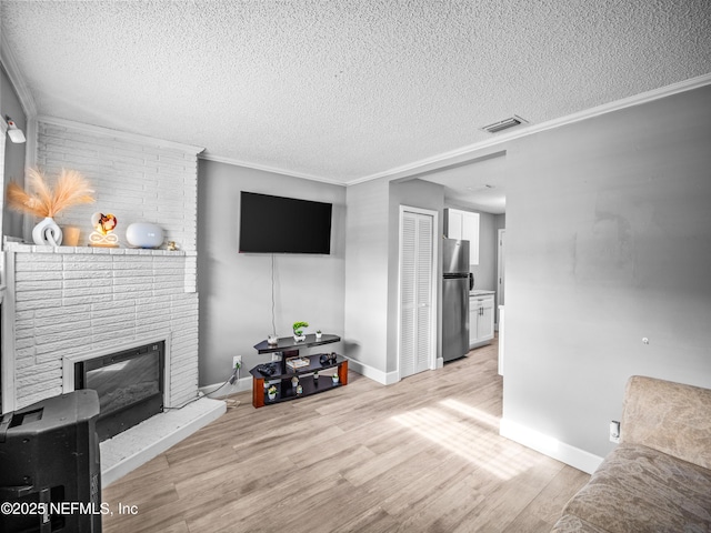 living room with crown molding, a brick fireplace, a textured ceiling, and light hardwood / wood-style floors