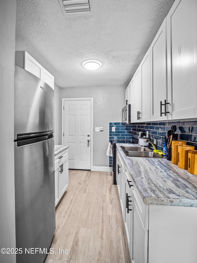 kitchen with sink, stainless steel appliances, tasteful backsplash, light hardwood / wood-style floors, and white cabinets