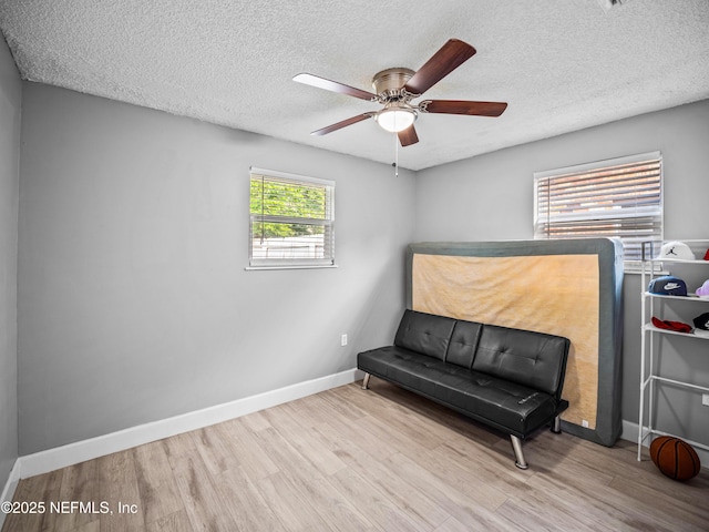 living area with ceiling fan, light hardwood / wood-style floors, and a textured ceiling