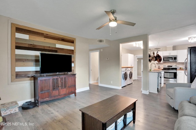 living room featuring ceiling fan, light wood-type flooring, sink, and washer and clothes dryer