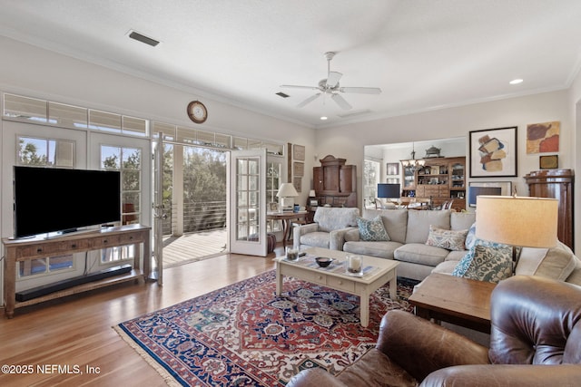 living room featuring crown molding, wood-type flooring, ceiling fan with notable chandelier, and french doors