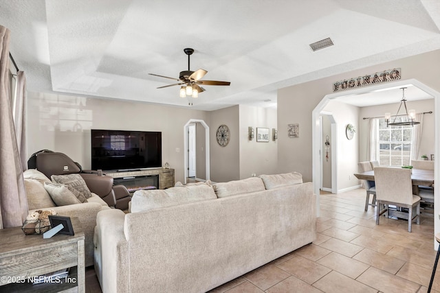 tiled living room featuring ceiling fan with notable chandelier and a raised ceiling