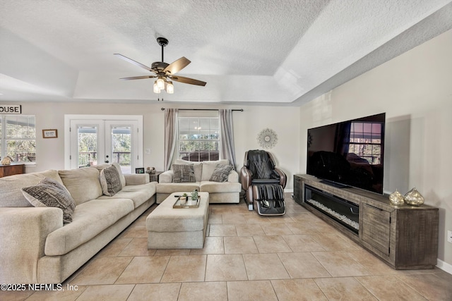 tiled living room featuring french doors, ceiling fan, a tray ceiling, and a textured ceiling