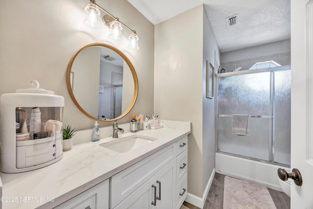 bathroom featuring vanity, combined bath / shower with glass door, and a textured ceiling