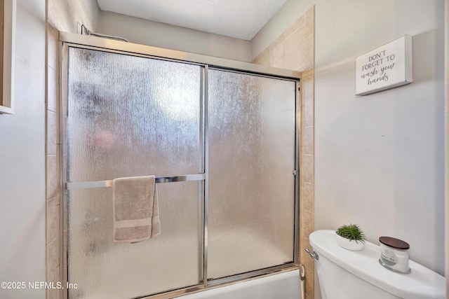 bathroom with toilet and shower / bath combination with glass door