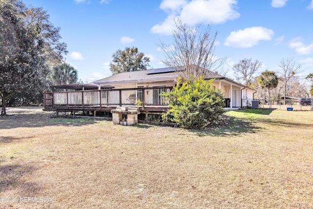 back of property with solar panels, a wooden deck, and a lawn