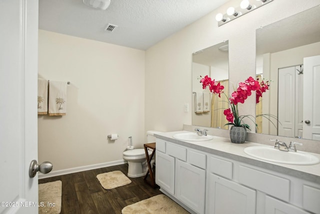 bathroom with hardwood / wood-style flooring, vanity, toilet, and a textured ceiling