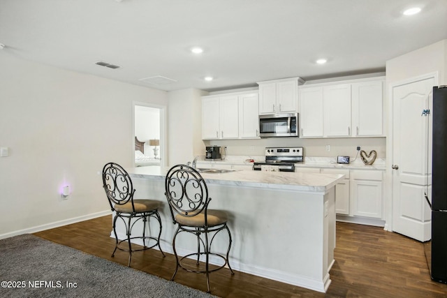 kitchen featuring an island with sink, appliances with stainless steel finishes, dark hardwood / wood-style floors, and white cabinets