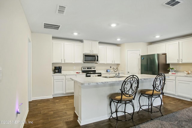 kitchen featuring appliances with stainless steel finishes, dark hardwood / wood-style floors, an island with sink, and white cabinets