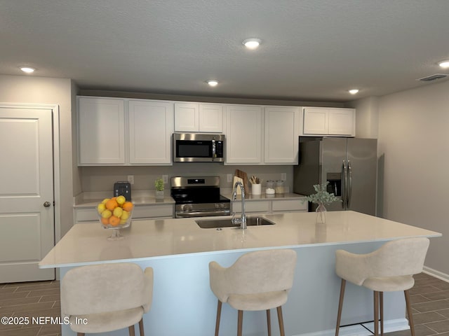 kitchen with a kitchen island with sink, a breakfast bar area, white cabinets, and appliances with stainless steel finishes