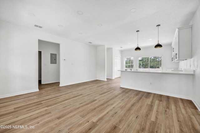 unfurnished living room with visible vents, baseboards, light wood-style floors, and electric panel