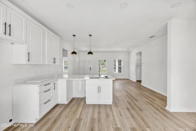 kitchen featuring white cabinets, a sink, light countertops, light wood-type flooring, and a peninsula