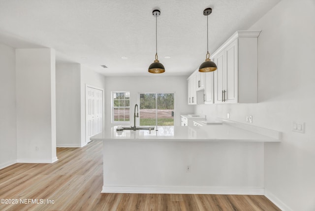 kitchen featuring a sink, light countertops, baseboards, and a peninsula
