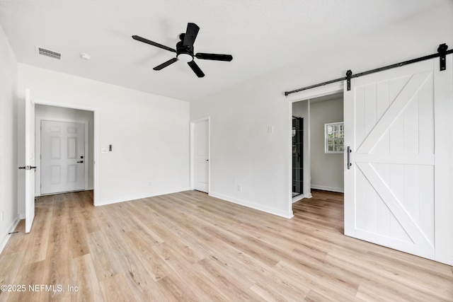 interior space with baseboards, a barn door, visible vents, ceiling fan, and light wood finished floors