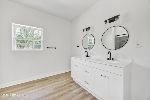 full bathroom featuring wood finished floors, double vanity, a sink, and baseboards