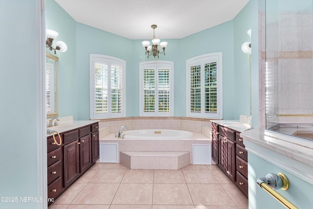 bathroom with tile patterned flooring, vanity, a relaxing tiled tub, and a notable chandelier