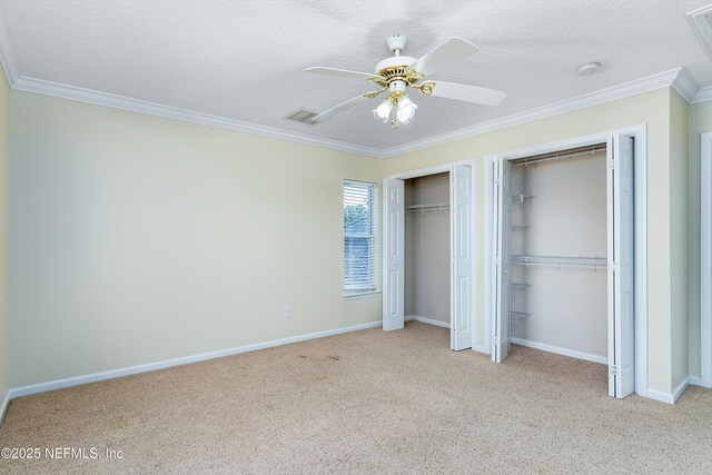 unfurnished bedroom featuring two closets, ornamental molding, ceiling fan, light carpet, and a textured ceiling