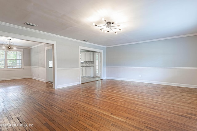 unfurnished living room featuring wood-type flooring, crown molding, and an inviting chandelier