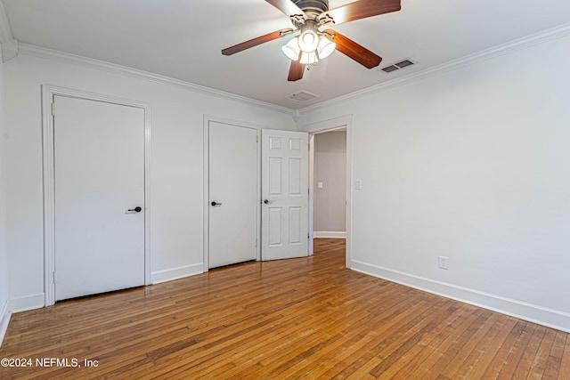 unfurnished bedroom with multiple closets, wood-type flooring, ornamental molding, and ceiling fan