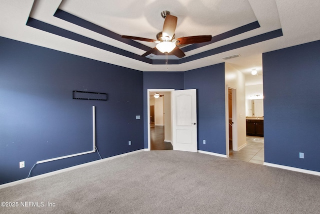 unfurnished bedroom with light carpet, a tray ceiling, ceiling fan, and ensuite bathroom