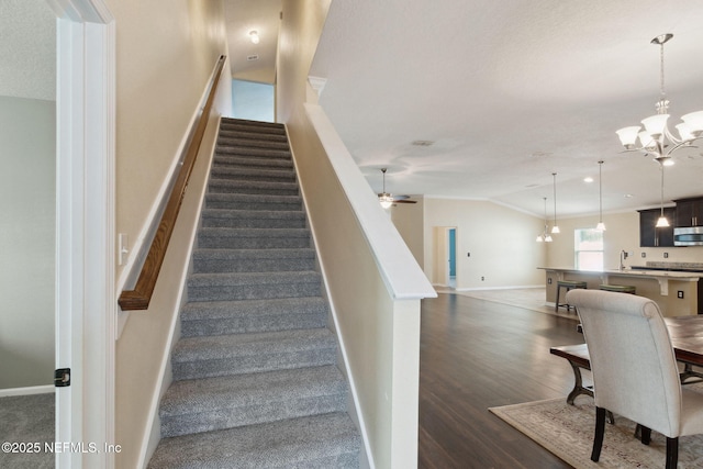 stairway featuring lofted ceiling, ceiling fan with notable chandelier, and wood-type flooring