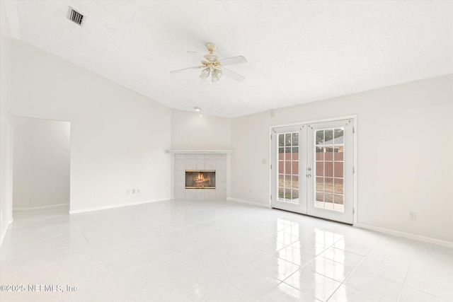 unfurnished living room featuring french doors, a textured ceiling, light tile patterned floors, ceiling fan, and a tiled fireplace