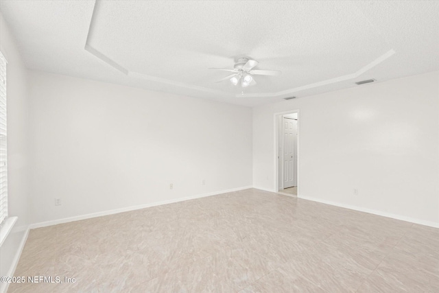 empty room with ceiling fan, a tray ceiling, and a textured ceiling