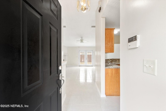 hall featuring sink, light tile patterned floors, an inviting chandelier, a textured ceiling, and french doors