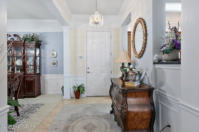 tiled foyer entrance with crown molding, an inviting chandelier, and decorative columns