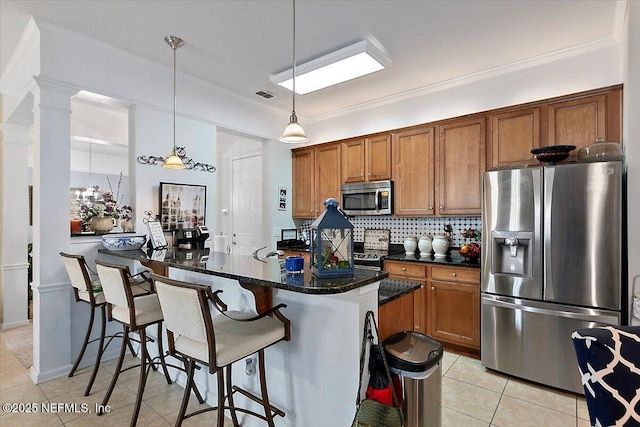 kitchen with decorative light fixtures, light tile patterned floors, appliances with stainless steel finishes, an island with sink, and backsplash