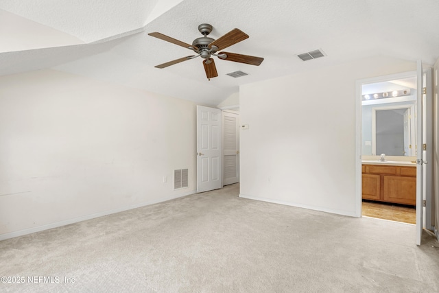 unfurnished bedroom with light colored carpet, sink, vaulted ceiling, and a textured ceiling