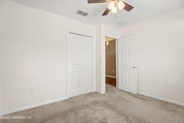 unfurnished bedroom with ceiling fan, light carpet, a textured ceiling, and a closet