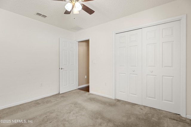 unfurnished bedroom featuring ceiling fan, light colored carpet, a closet, and a textured ceiling