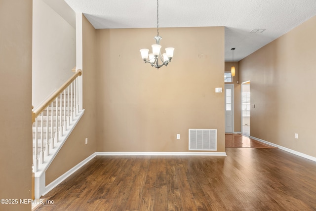 empty room featuring dark wood-type flooring, an inviting chandelier, and a textured ceiling