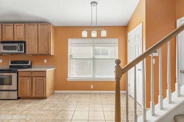 kitchen featuring pendant lighting, stainless steel appliances, light tile patterned flooring, and a textured ceiling