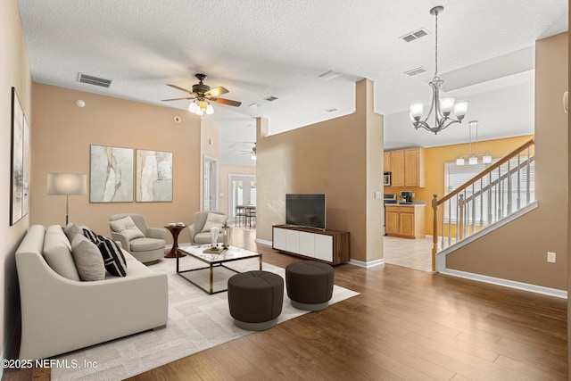 living room featuring ceiling fan with notable chandelier, a textured ceiling, and light wood-type flooring