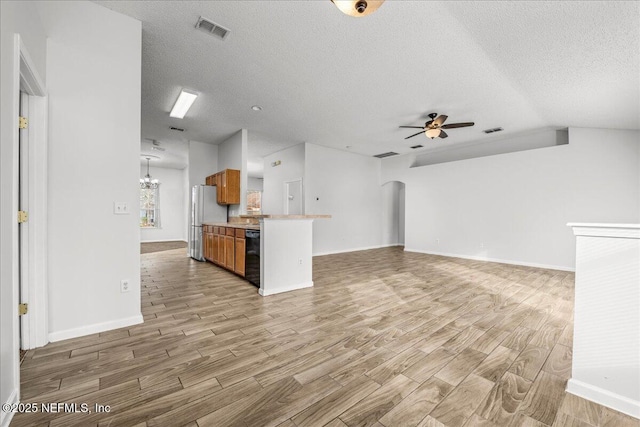 unfurnished living room with ceiling fan with notable chandelier, vaulted ceiling, a textured ceiling, and light wood-type flooring