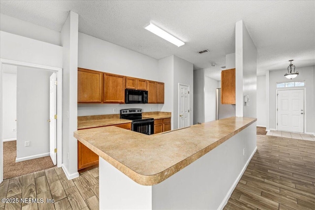 kitchen with decorative light fixtures, a textured ceiling, kitchen peninsula, light hardwood / wood-style floors, and black appliances