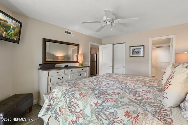 bedroom with ensuite bath, wood-type flooring, stainless steel fridge, a closet, and ceiling fan