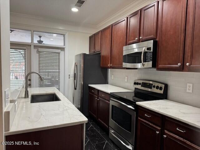 kitchen featuring sink, appliances with stainless steel finishes, backsplash, ornamental molding, and light stone countertops